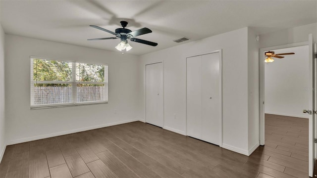 unfurnished bedroom featuring multiple closets, visible vents, baseboards, and wood finished floors