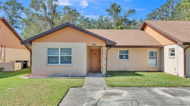 view of front of home with a shingled roof, a front yard, and stucco siding