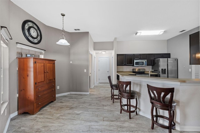 kitchen featuring kitchen peninsula, a breakfast bar, pendant lighting, appliances with stainless steel finishes, and light hardwood / wood-style floors