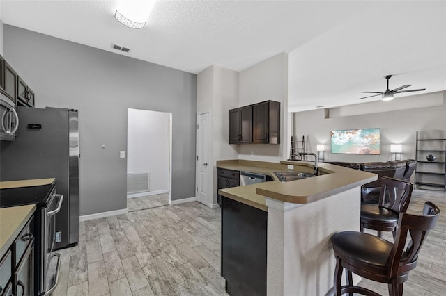 kitchen featuring kitchen peninsula, dark brown cabinets, appliances with stainless steel finishes, a breakfast bar, and sink