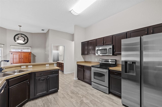 kitchen with light hardwood / wood-style flooring, dark brown cabinets, sink, pendant lighting, and appliances with stainless steel finishes