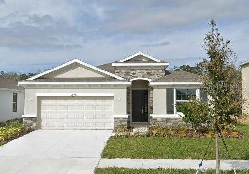 single story home featuring an attached garage, stone siding, concrete driveway, stucco siding, and a front yard