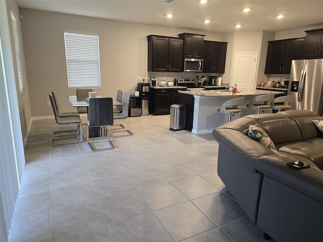 kitchen with a breakfast bar area, an island with sink, light tile patterned flooring, appliances with stainless steel finishes, and light stone counters