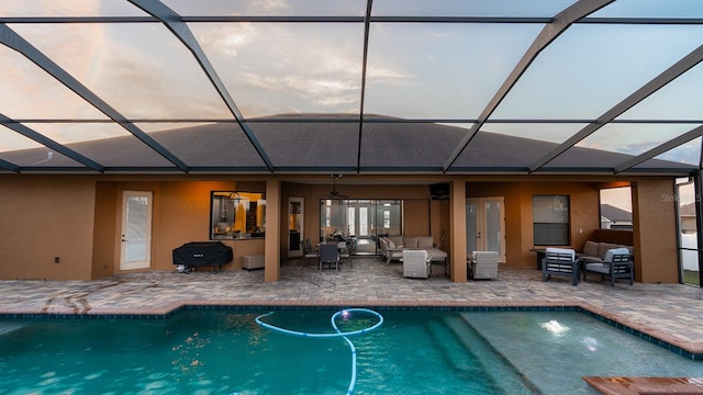 pool at dusk featuring an outdoor hangout area, grilling area, glass enclosure, and a patio