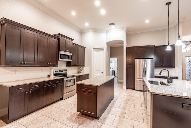 kitchen featuring stainless steel appliances, dark brown cabinetry, a center island with sink, sink, and decorative light fixtures