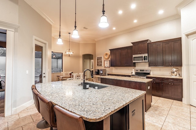 kitchen featuring stainless steel appliances, dark brown cabinetry, sink, decorative light fixtures, and a kitchen island with sink