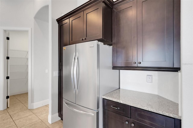 5074 Shore Side Dr, Lakeland, FL 33812 - kitchen featuring freestanding refrigerator, dark brown cabinetry, light tile patterned flooring, baseboards, and light stone countertops