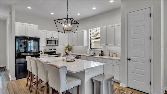 kitchen with a kitchen island, light hardwood / wood-style flooring, white cabinets, pendant lighting, and appliances with stainless steel finishes