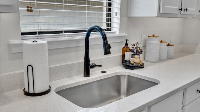 interior details with white cabinetry, sink, and light stone counters