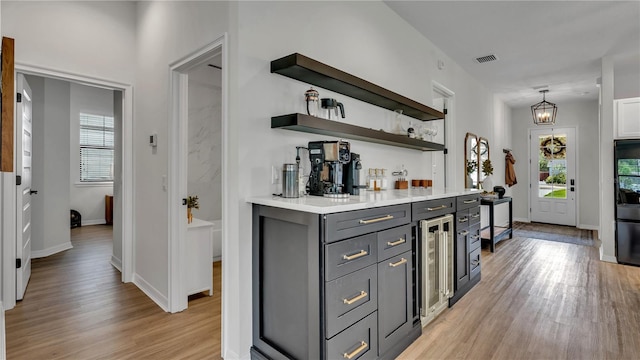 bar with wine cooler, decorative light fixtures, light wood-type flooring, and gray cabinets