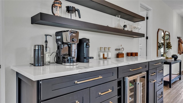 bar with gray cabinets, light stone countertops, light wood-type flooring, and beverage cooler