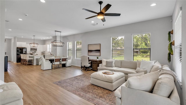 living room with light hardwood / wood-style floors and ceiling fan with notable chandelier