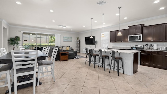 kitchen with light stone countertops, decorative light fixtures, a center island with sink, appliances with stainless steel finishes, and a kitchen breakfast bar