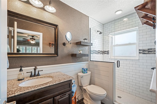 bathroom with ceiling fan, vanity, a textured ceiling, a shower with shower door, and toilet