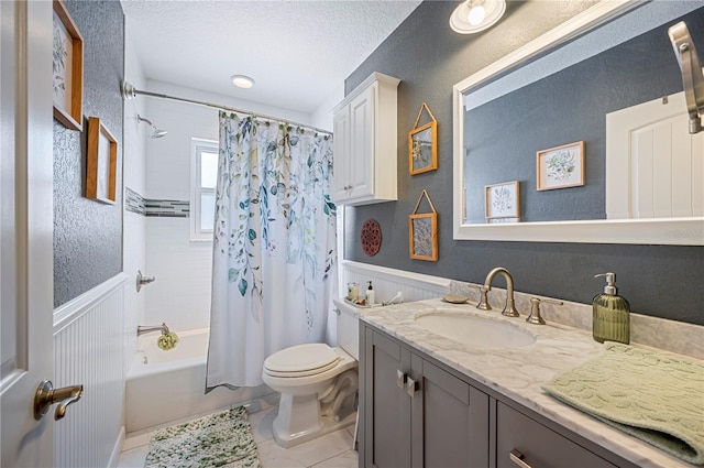 bathroom featuring toilet, vanity, shower / bath combo with shower curtain, wainscoting, and a textured ceiling