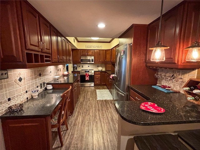 kitchen with a kitchen bar, hanging light fixtures, appliances with stainless steel finishes, dark hardwood / wood-style floors, and kitchen peninsula