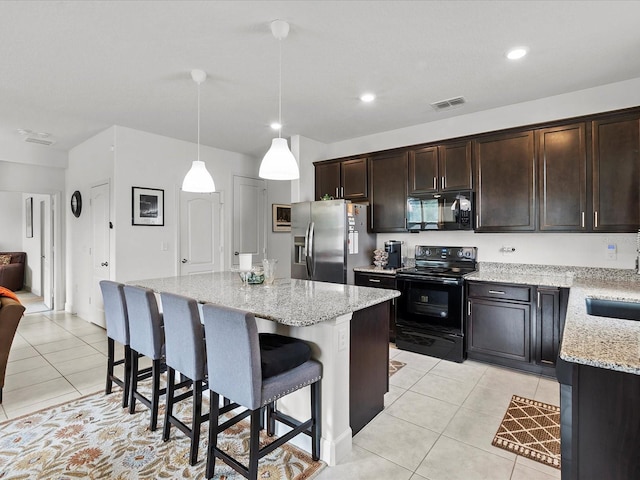 kitchen featuring pendant lighting, a center island, black appliances, light stone countertops, and light tile patterned floors