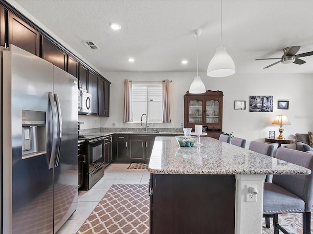 kitchen featuring pendant lighting, appliances with stainless steel finishes, a kitchen island, light stone counters, and a breakfast bar area