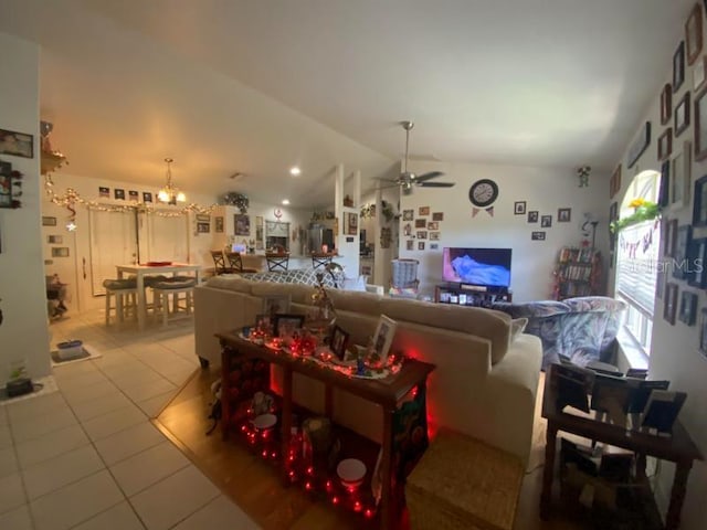 tiled living room with ceiling fan with notable chandelier and lofted ceiling