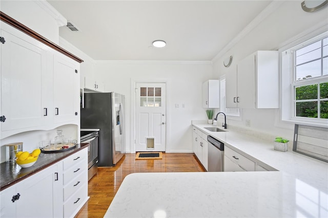 kitchen with sink, white cabinetry, light hardwood / wood-style floors, stainless steel appliances, and crown molding