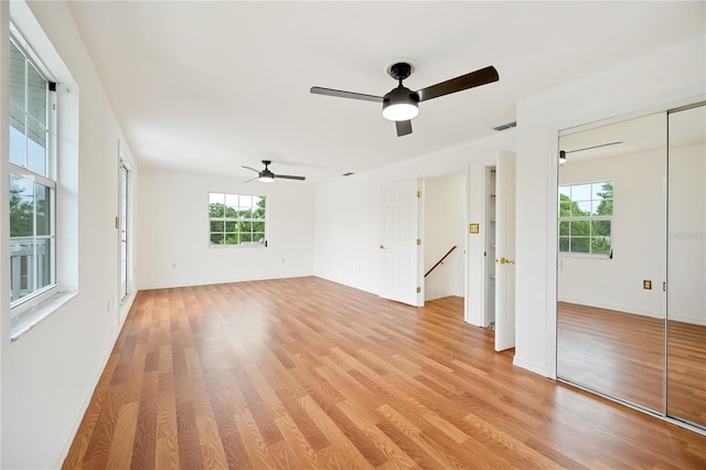 empty room with ceiling fan, a wealth of natural light, and light wood-type flooring