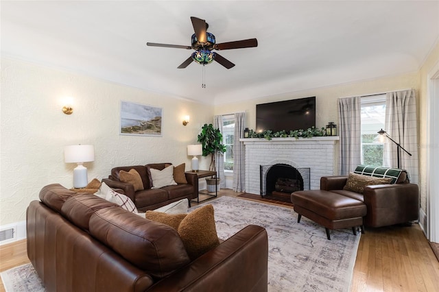 living room with light hardwood / wood-style flooring, a brick fireplace, and ceiling fan