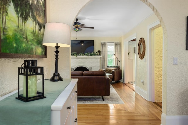 living room with a brick fireplace, light wood-type flooring, and ceiling fan