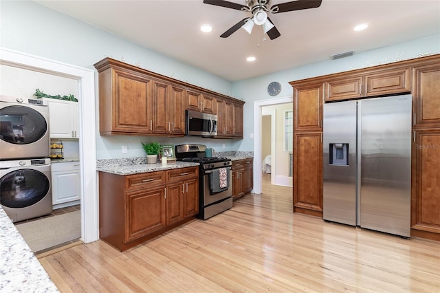 kitchen featuring light wood-type flooring, ceiling fan, stainless steel appliances, light stone counters, and stacked washer and clothes dryer