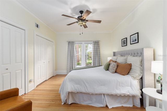 bedroom with multiple closets, crown molding, light wood-type flooring, and ceiling fan