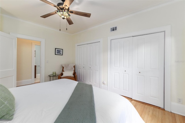 bedroom featuring ornamental molding, two closets, hardwood / wood-style flooring, and ceiling fan