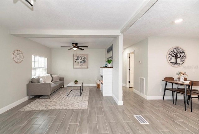 living room with light hardwood / wood-style flooring, a textured ceiling, beamed ceiling, and ceiling fan