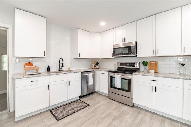 kitchen featuring stainless steel appliances, light stone countertops, sink, and white cabinets