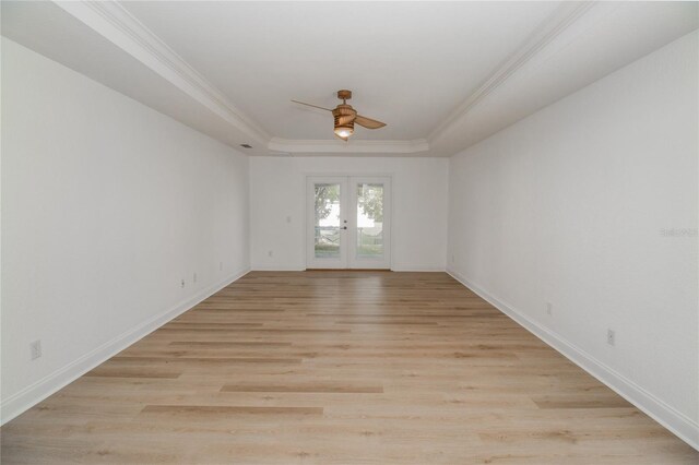 empty room featuring ornamental molding, a tray ceiling, and light wood-type flooring