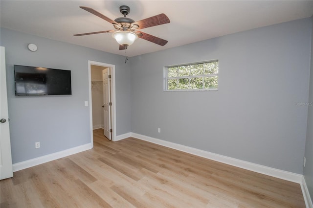 unfurnished bedroom featuring a spacious closet, light hardwood / wood-style floors, a closet, and ceiling fan