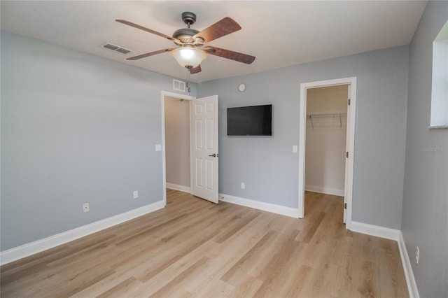 unfurnished bedroom featuring a closet, light hardwood / wood-style flooring, a spacious closet, and ceiling fan