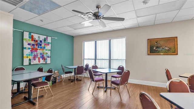 dining space with ceiling fan, a drop ceiling, and hardwood / wood-style floors