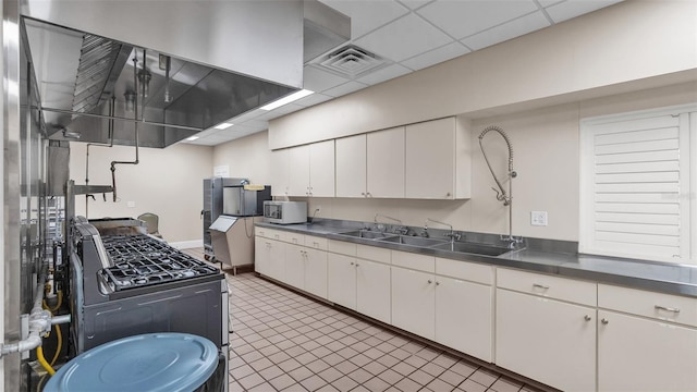 kitchen with dark tile patterned flooring, black range with gas cooktop, sink, white cabinetry, and a paneled ceiling