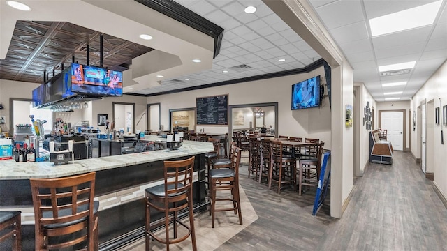 bar with light stone counters, wood-type flooring, and ornamental molding