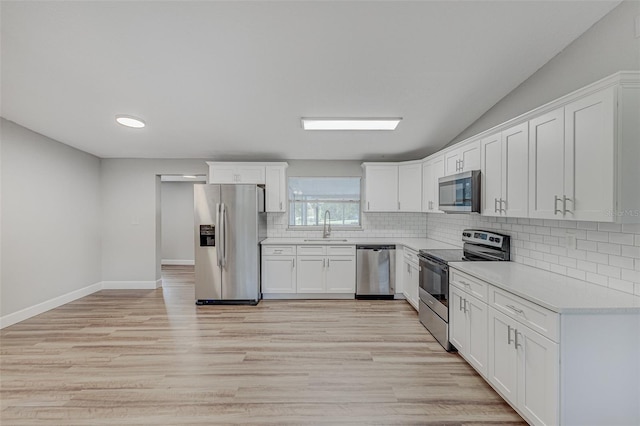 kitchen with white cabinets, backsplash, appliances with stainless steel finishes, light hardwood / wood-style floors, and sink