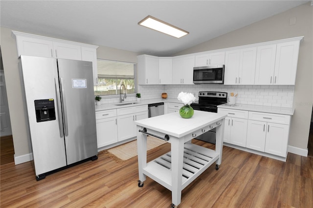 kitchen with vaulted ceiling, white cabinetry, sink, decorative backsplash, and stainless steel appliances