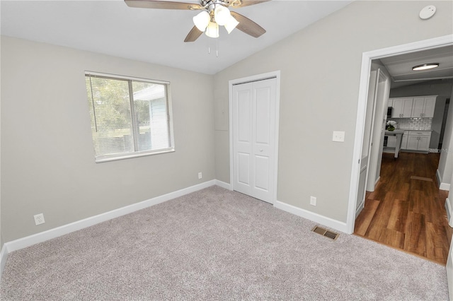 unfurnished bedroom with dark carpet, ceiling fan, vaulted ceiling, and a closet