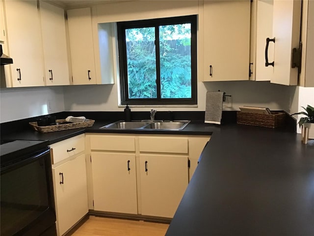 kitchen featuring black electric range oven, sink, light wood-type flooring, and white cabinets