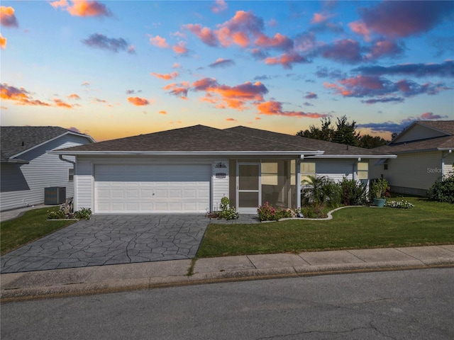 single story home featuring a yard, a garage, and central air condition unit