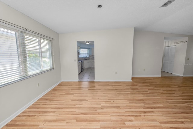 unfurnished room with lofted ceiling, a textured ceiling, and light hardwood / wood-style floors