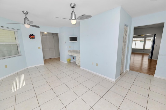 spare room with built in desk, light hardwood / wood-style floors, and ceiling fan