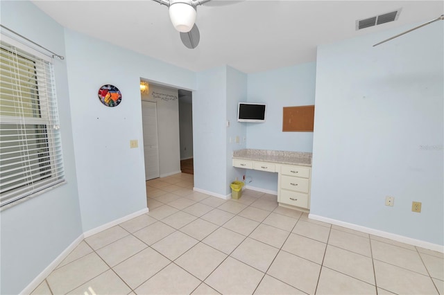 unfurnished bedroom featuring built in desk, ceiling fan, and light tile patterned floors