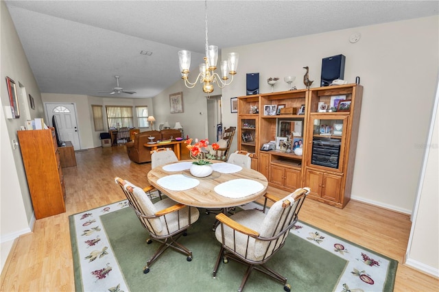 dining area featuring a textured ceiling, vaulted ceiling, ceiling fan with notable chandelier, and light hardwood / wood-style floors