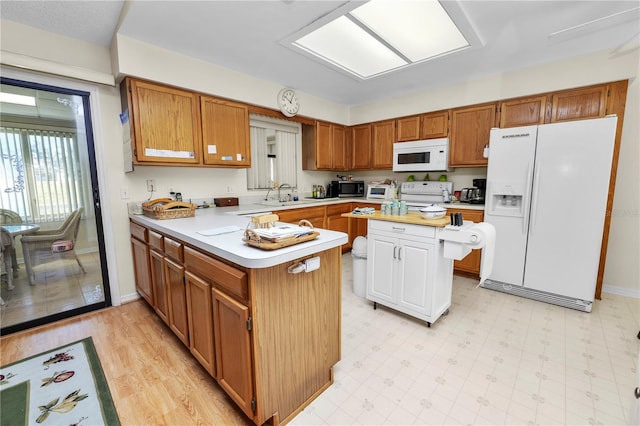 kitchen featuring white appliances, sink, a kitchen island, kitchen peninsula, and light hardwood / wood-style flooring