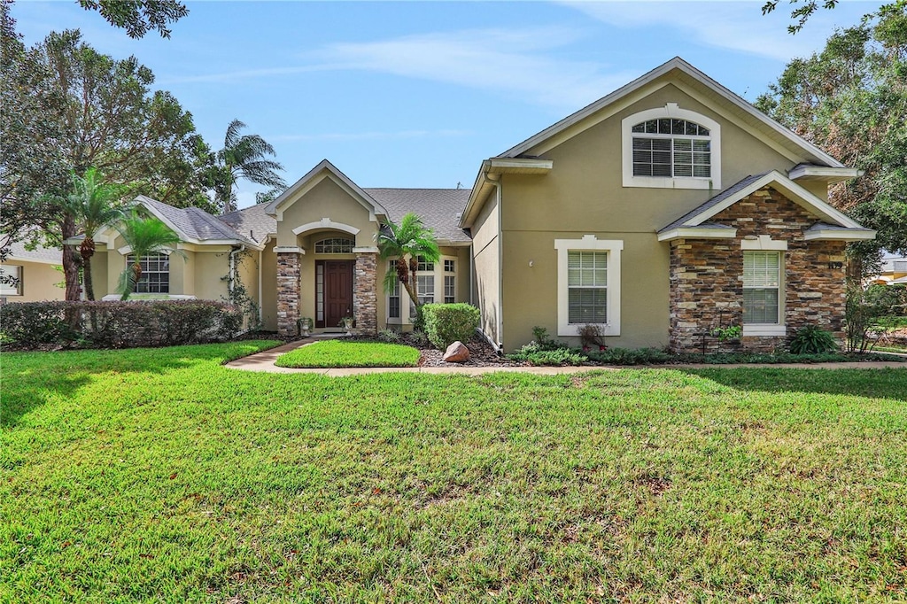 view of front of home with a front yard, stone siding, and stucco siding