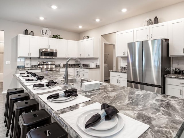 kitchen featuring a kitchen breakfast bar, white cabinets, stainless steel appliances, and dark stone counters